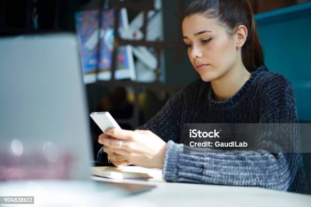Concentrated Female Hipster Sharing Multimedia Files In Social Networks Using Wireless Connection And Smartphone Serious Young Student Checking Email Box Texting Messages On Telephone In Coworking Stock Photo - Download Image Now