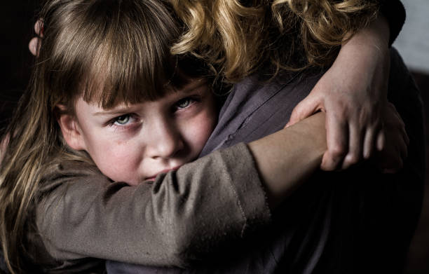 Girl hugging mother. Photo shooting indoors. On the background of a white brick wall . Child ( girl ) hugs his mother. family mother poverty sadness stock pictures, royalty-free photos & images