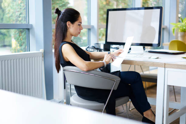 istock Confident female entrepreneur reading text of contract analyzing financial information sitting in cabinet near computer blank screen, prosperous attractive lawyer concentrated on documentation 904848550