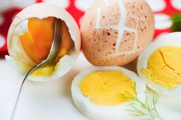 Hard boiled eggs, one with cracked shell, sliced and spoon in yolk.