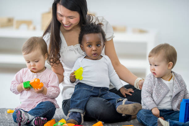 Child Care Worker A group of babies are sitting with their babysitter on the carpet. The babies are playing with colorful toy blocks. asian nanny stock pictures, royalty-free photos & images