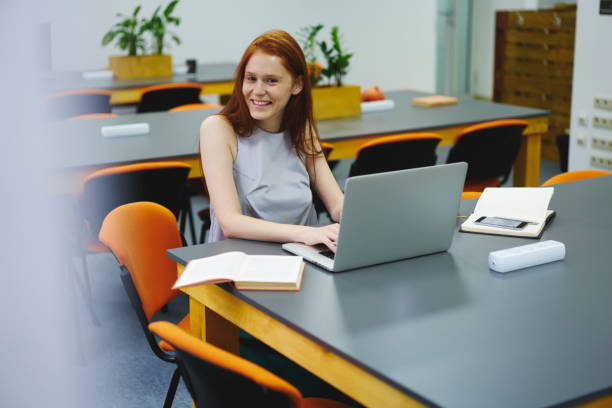 istock Half length portrait of foxy pretty student looking at camera and laughing while chatting with followers via laptop computer connected to wireless internet sitting in library during work break 904850208