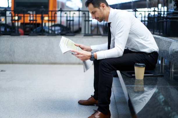 istock Handsome financial manager concentrated on reading business article while waiting for public transport in railway station, prosperous banker spending time on coffee break on analyzing printed media 904852452
