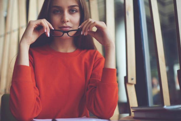 istock Attractive intelligent hipster girl looking at camera while holding stylish optical spectacles in hands for better vision.Half length portrait of smart student using eyeglasses with trendy black frame 904857536
