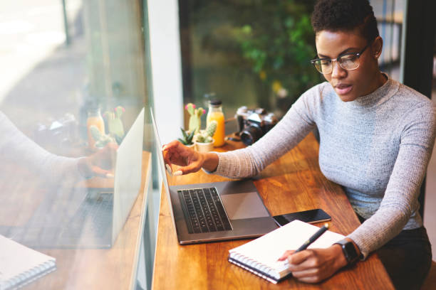 istock Concentrated afro american freelancer making notes of information from internet sitting in cafe interior, prosperous owner in trendy eyewear of online store writing report organising working process 904867674