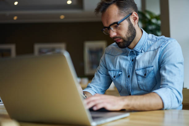 istock Cropped image of male it developer installing software on modern laptop connecting to wireless 4G internet.Pensive freelancer in optical spectacles typing text on keyboard of computer sitting indoors 904869266