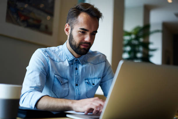 istock Concentrated handsome freelancer reading email on laptop device connected to wireless 4G internet.Smiling bearded copywriter dressed in denim shirt working at computer sitting in coworking space 904871402