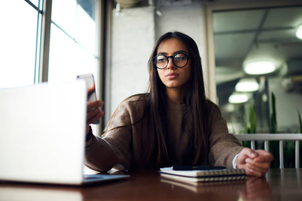 istock Young concentrated administrative manager in trendy eyeglasses paying for receipt transfer money on laptop computer and confirming banking operations sending feedback using modern smartphone 904873278
