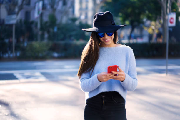 istock Smiling trendy dressed female hipster enjoying walking on town streets while texting messages via smartphone, charming tourist in stylish hat and sunglasses using online maps for making city tour 904876776