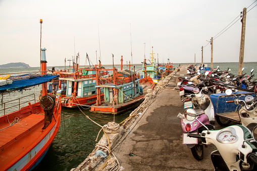 Colorful fishing boats at harbor in Ang Sila, Thailand, Asia. Lots of motor bikes on the pier