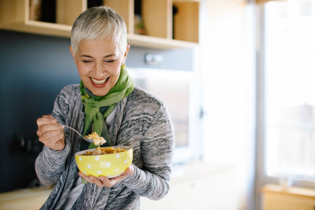 femme mature prenant son petit déjeuner sain - muesli photos et images de collection