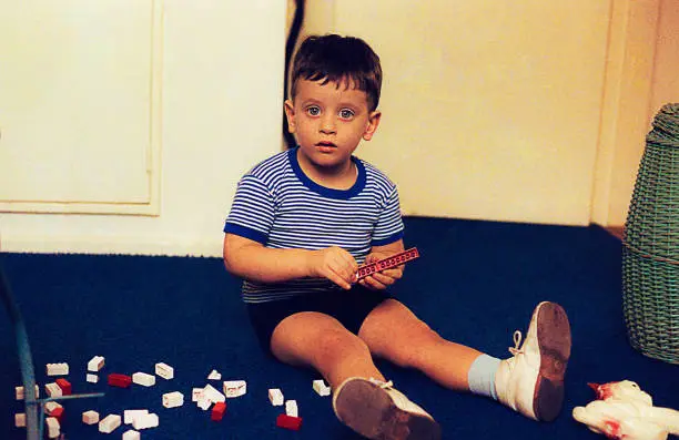 vintage photo from the seventies of a child sitting on the floor, playing and looking at camera with big blue eyes.