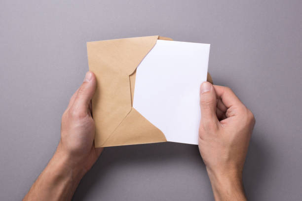 istock Man holds a mock-up letter or postal card with an envelope on a gray background. A man takes out or puts a letter 904881282