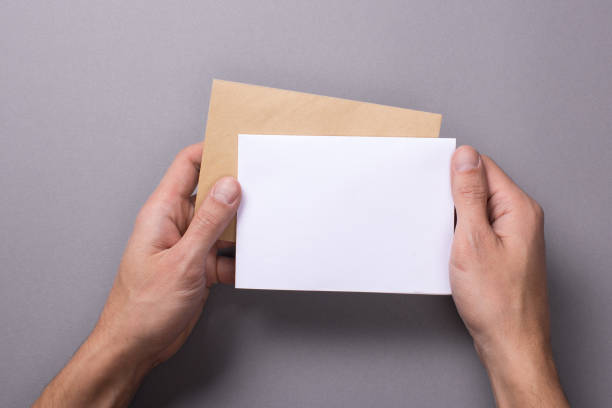 istock Man holds a mock-up letter or postcard in his hands with envelope on a gray background 904881292