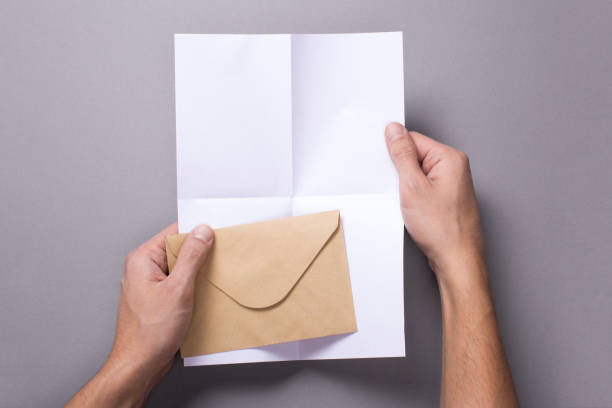 istock Man holds an open blank letter mock-up and and envelope on a gray background 904881324