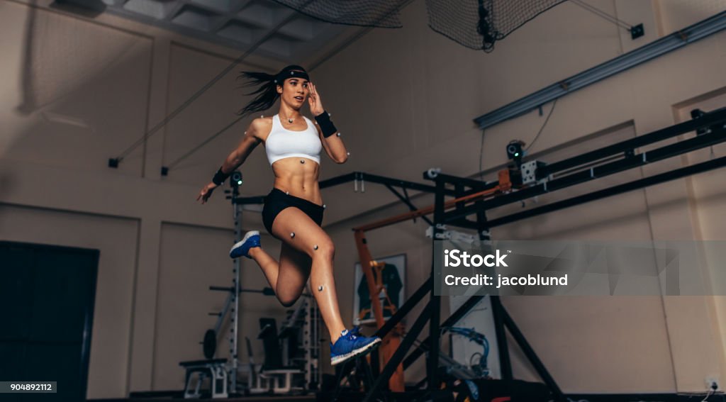 Movement and performance monitoring of runner in biomechanical lab Female athlete with motion capture sensors on her body running in biomechanical lab. Recording the movement and performance of sportswoman in sports science lab. Sport Stock Photo