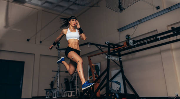 Movement and performance monitoring of runner in biomechanical lab Female athlete with motion capture sensors on her body running in biomechanical lab. Recording the movement and performance of sportswoman in sports science lab. biomechanics stock pictures, royalty-free photos & images