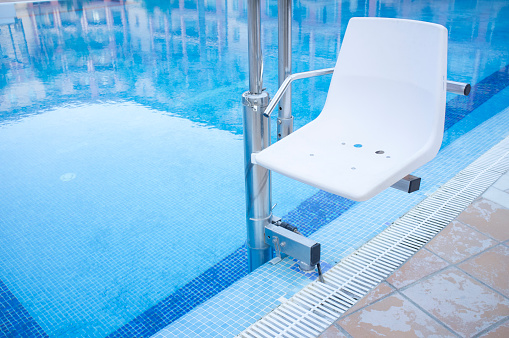 Swimming pool lift for disabled people access to the pool. Holidays resort background