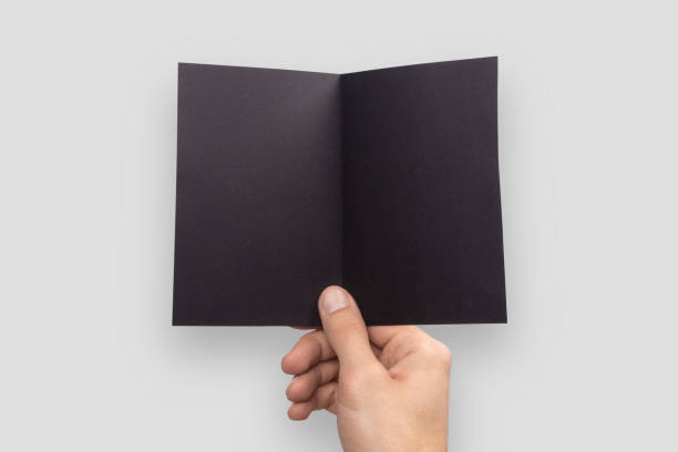 istock Mockup A6 empty blank black postcard horizontally bent in half holds the man in his hand. Isolated on a gray background 904905916