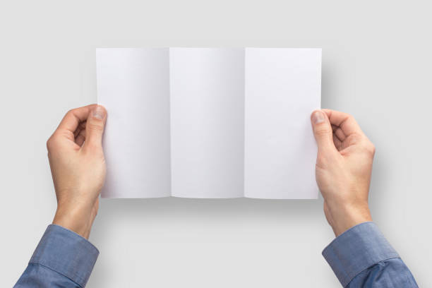 istock Mockup flaeth folded three times empty blank white holds the man in his hand in shirt. Isolated on a gray background 904906078