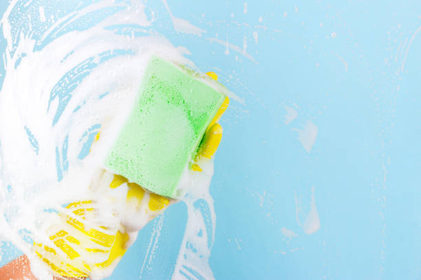 istock Washing windows and glass. The worker in a yellow glove can stack a sponge with foam on a blue background 904909202