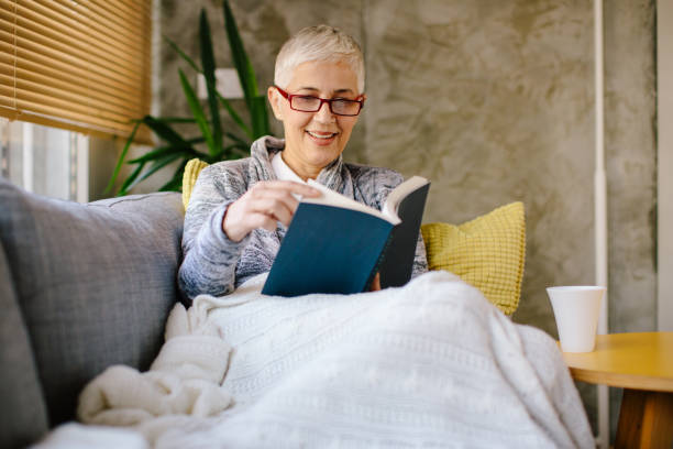 istock Mature woman resting on sofa and reading book 904912656