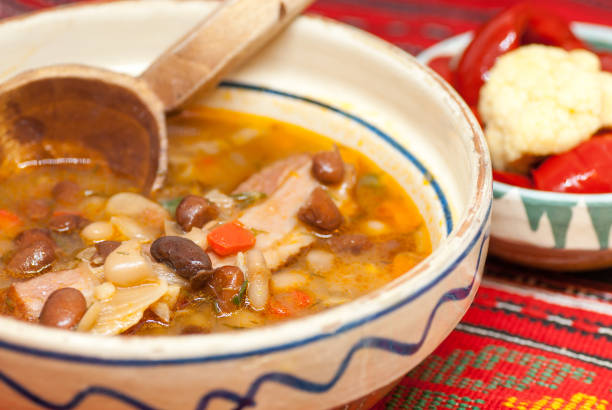 Top view of a white bowl filled with bean and carrot soup with a spoon in the food on an old wood table.