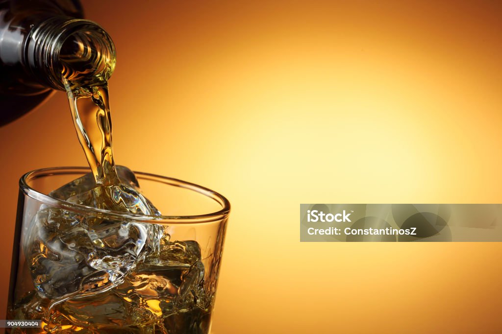 pouring whiskey closeup of pouring whiskey against orange gradient Alcohol - Drink Stock Photo