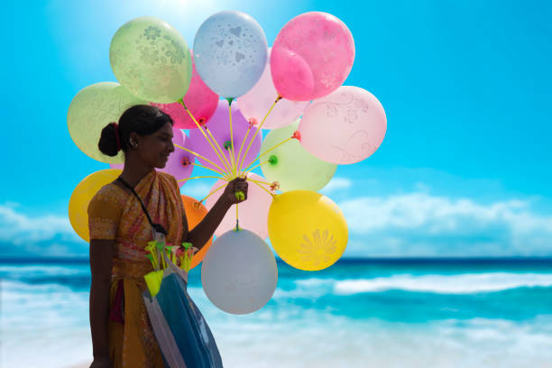 Indian hawker selling colorful balloons at a beach.