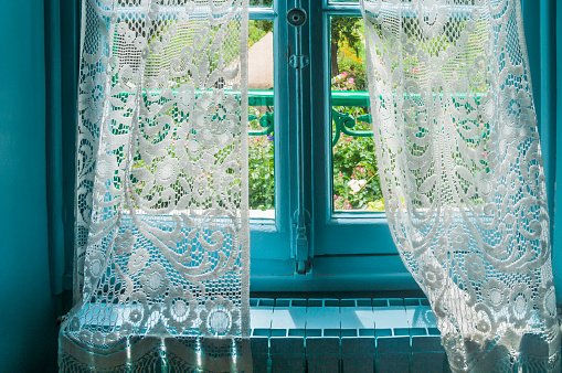White lace curtains are slightly pulled aside to reveal a garden beyond