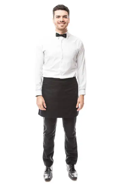 Full length portrait of a good looking waiter wearing a bowtie and an apron