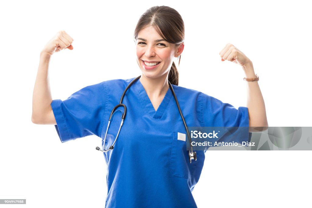 Female doctor acting as superhero Pretty Hispanic female doctor wearing scrubs and flexing her arms acting like a superhero Nurse Stock Photo