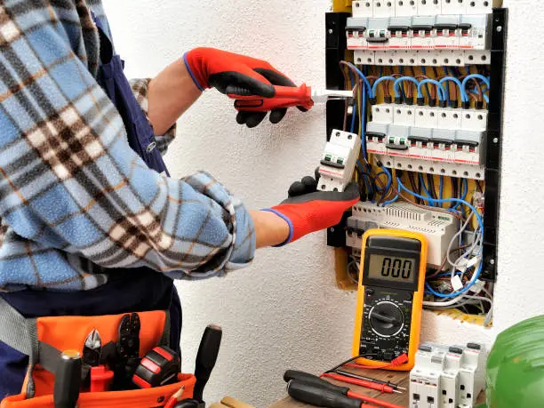 Photo of Young electrician technician at work on a electrical panel with protective gloves