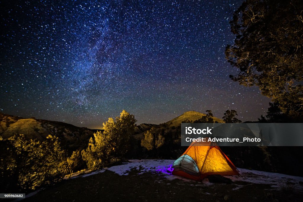 Camping in a Tent Under the Stars and Milky Way Galaxy Camping in a Tent Under the Stars and Milky Way Galaxy - Scenic landscape with hils and mountains with orange glowing tent in dark with view of night sky with Milky Way and bright stars. Camping Stock Photo