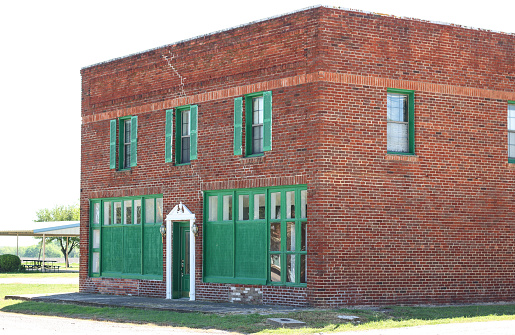 perspective of an old red brick building exterior with green shutters and green doorway on a bright sunny day