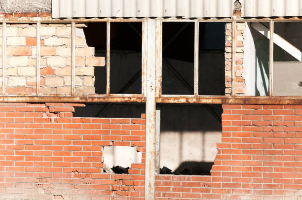 istock Damaged warehouse exterior wall with broken glass windows destroyed in war close up 904991756
