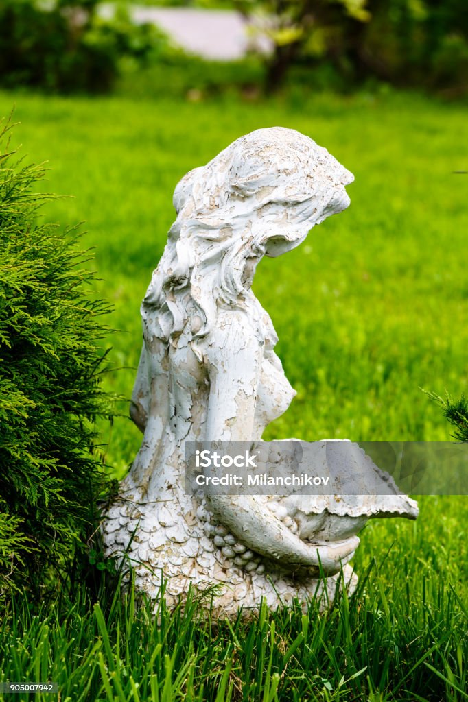 Old statue of a seated girl in a Park in the grass. Adult Stock Photo