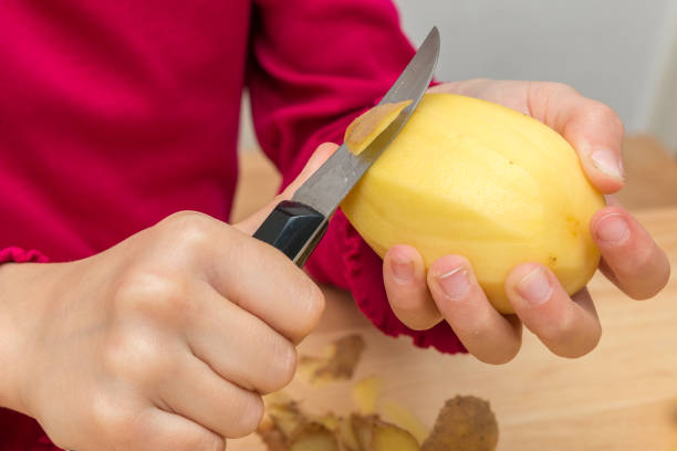 Close-up of two children's hands peeling a potato with a sharp kitchen knife or peeling knife