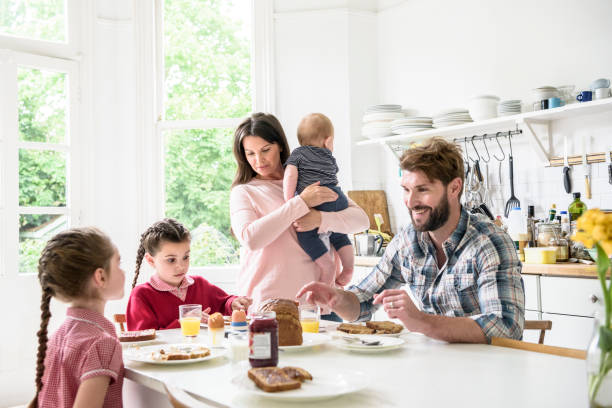 istock Mother holding baby as father sits and eats breakfast with daughters around kitchen table 905028596