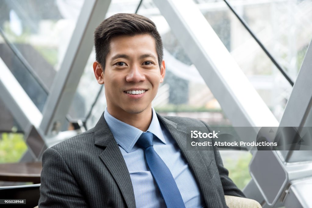 Young smiling handsome Asian Thai-Chinese businessman Young smiling handsome Asian Thai-Chinese businessman sitting at office lounge Businessman Stock Photo