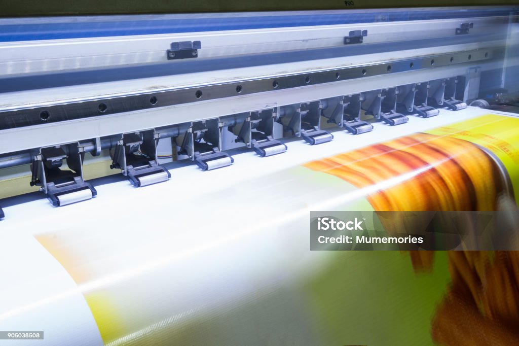 Format large inkjet printer working on vinyl banner Format large inkjet printer working on yellow vinyl banner Printing Plant Stock Photo