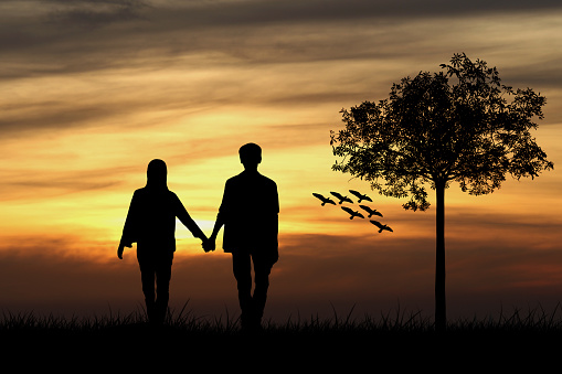 Silhouette of couple man and woman at tree and birds with sunset background, love concept.