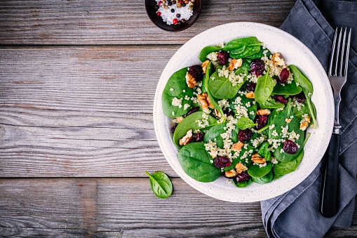 Green salad bowl with spinach, quinoa, walnuts and dried cranberries on wooden background