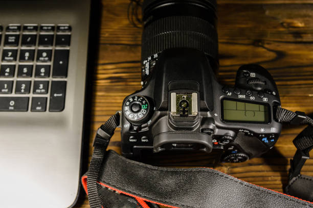 istock Modern DSLR camera and laptop on wooden table. Top view 905106150