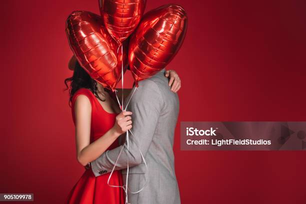 Couple Covering Faces With Bundle Of Balloons Isolated On Red Stock Photo - Download Image Now