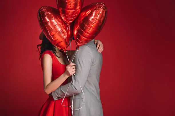 couple covering faces with bundle of balloons isolated on red