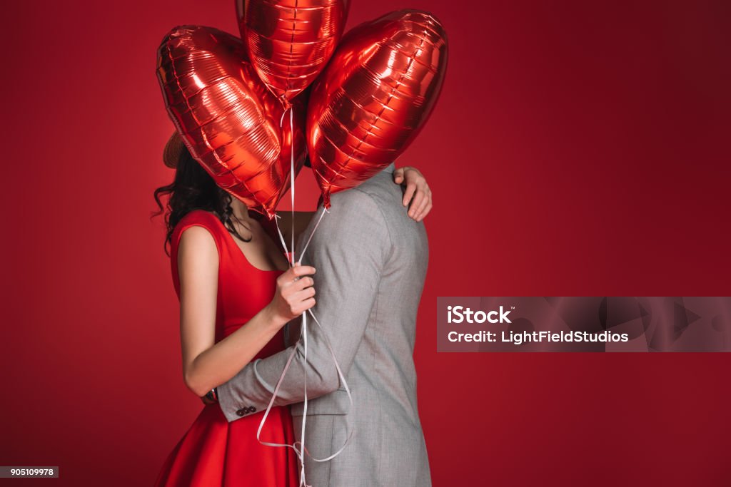casal cobrindo rostos com pacote de balões isolado no vermelho - Foto de stock de Dia dos Namorados royalty-free