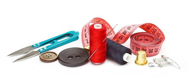 Sewing supplies and accessories for needlework. Fabric, spools of thread, scissors and thimbles on white background.
