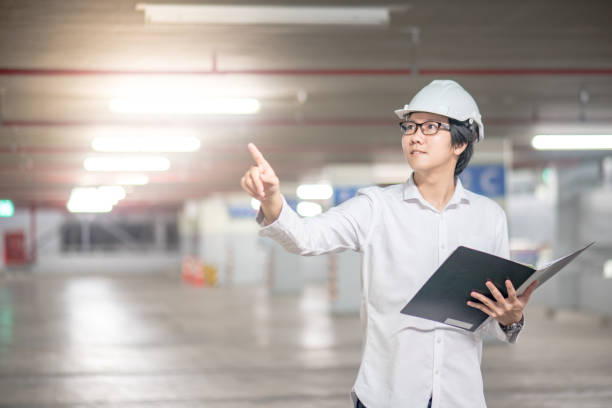 istock Young Asian Engineer or Architect holding files and pointing his hand at construction site 905118890