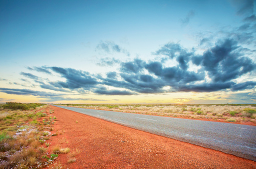 A long, straight bitumen road makes its way through the dry, red desert.